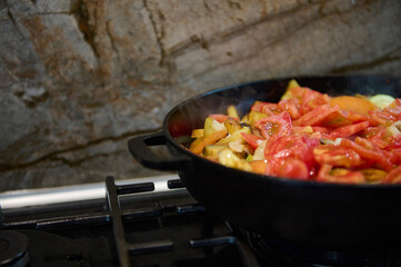 Partial view of fresh chopped organic ingredients fried in a cast iron skillet on a stovetop in a...