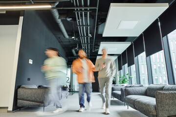 Fototapeta na wymiar motion blur of modern entrepreneurs in casual clothes walking along lounge corridor with comfortable couches in coworking office with high tech interior, movement, collaboration, dynamic business