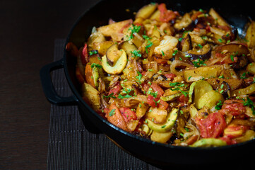 Freshly cooked vegetable stew of seasonal veggies in a cast-iron skillet, on a wooden background. Vegetarian tasty meal
