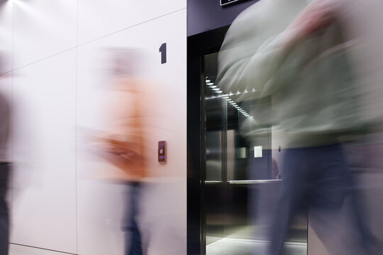 Long Exposure Of Business People Walking Near Elevator With Open Doors In Contemporary Coworking Office With High Tech Interior, Movement, Dynamic Business, Productivity