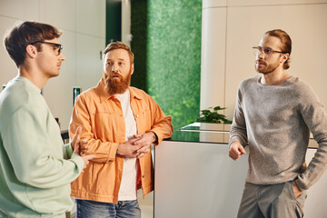 thoughtful bearded man in stylish casual clothes looking at serious business partners discussing...