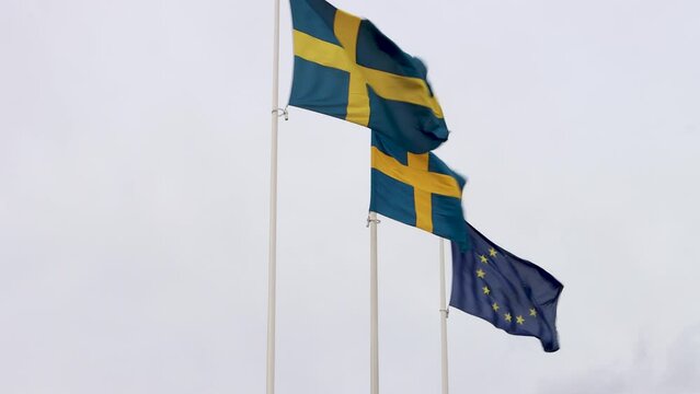 European Union (EU) and Sweden flags move in wind by cloudy sky