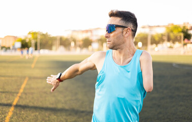An adult senior soccer player stretches out an arm in the middle of a soccer field. The man is wearing sports glasses and a tank top. Concept of disabled footballers, athletes with an amputated arm.