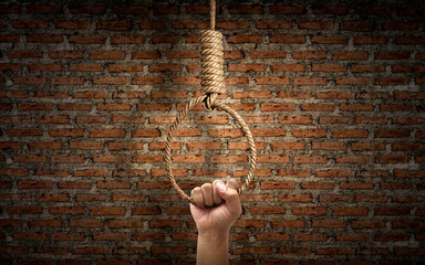 Hand holding rope noose with hangman's knot hanging on dark brick wall
