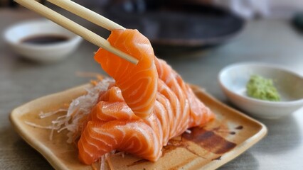 Chopsticks holding salmon sashimi. Salmon Sashimi and wasabi on disc.