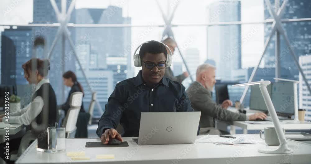 Poster succesful black man puts on headphones and starts typing on laptop computer in skyscraper office in 