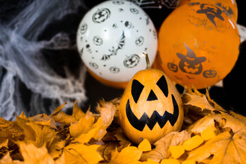 Halloween's holiday attributes. Lantern carved from pumpkin known as Jack-o-lantern on a black background with spider webs, autumn leaves and balloons. Trick or treat