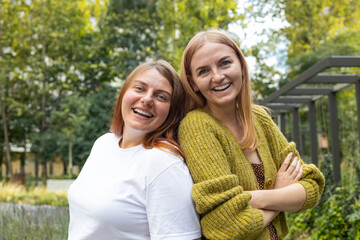 Cheerful girls embracing each other. Image of two young happy women friends standing outdoors at summer park. Looking at camera. High quality photo