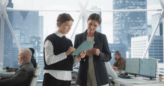 Professional Female Lawyer And Her Assistant Standing In Modern Diverse Skyscraper Office In Downtown. Two Caucasian Woman Going Through Schedule and Meetings With Clients On Tablet In Law Firm.
