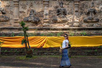 Pretty Asian tourists woman wearing beautiful hand-woven clothes dyed with indigo and mud-fermented natural colors modern Thai traditional dress costumes are popular in ancient temple Thailand.