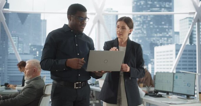 Businesspeople in Modern Office: Business Meeting of Two Managers Using Laptop. Female CEO and African American Operations Director Talk, Discuss Strategy, Implementing Marketing and Financial Plans.