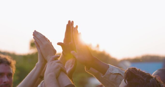 Multiracial group of diverse young people giving high five against a setting sun, feels excited close up focus on stacked palms during golden hour. Respect and trust, celebration and friendship