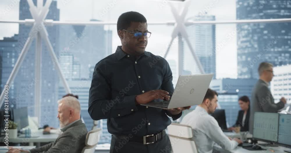 Poster Handsome African American CEO Walking In Modern Skyscraper Office With Diverse Employees In Downtown. Succeful Black Man Using Laptop Computer To Go Through Tasks And Business Meetings In Tech Startup
