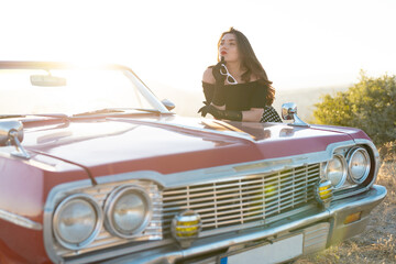 beautiful girl in retro style posing near vintage red cabriolet car.