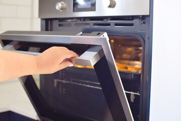 A woman opens the glass door of a modern built-in oven.  Cooking at home.