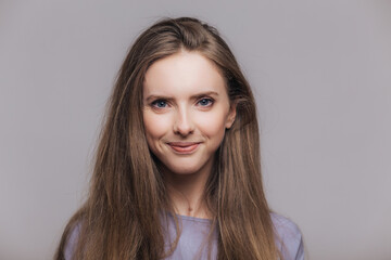 Content brunette model with blue eyes, isolated on grey. Studio shot of delighted woman.