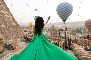 a girl in a flying dress with a long train on the background of balloons in Cappadocia.