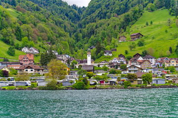 Fototapeta na wymiar Scenic view of village Sisikon at lakeshore of lake Lucerne seen from viewpoint of Swiss path hiking trail on a cloudy spring day. Photo taken May 18th, 2023, Seelisberg, Switzerland.