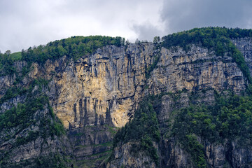 Naklejka premium Scenic landscape with cliff and woodland at lakeshore of Lake Lucerne seen from passenger ship on Lake Lucerne on a cloudy spring day. Photo taken May 18t, 2023, Treib, Canton Uri, Switzerland. 