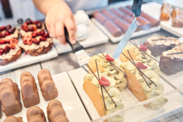 A showcase in a pastry shop with delicious desserts with fresh berries and cream. A variety of cakes covered with chocolate and decorated with pistachio mousse. Delicious pastries in the coffee shop. 