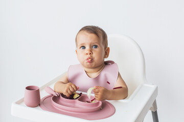 Child small and cute close-up portrait sits in a highchair on a white background and eats complementary foods, choked.