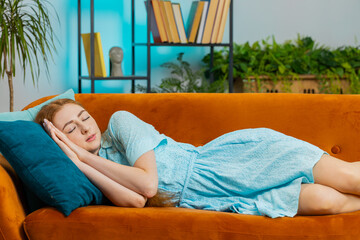 Tired young redhead woman lying down in bed taking a rest at home. Portrait of carefree girl napping, falling asleep on comfortable orange sofa with pillows. Closed her eyes enjoy daytime nap alone - Powered by Adobe