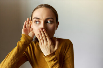 Horizontal portrait of shocked girl covering mouth looking aside with big round eyes eavesdropping rumors or gossips, after hearing shocking news. Emotions, feelings, body language