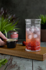 
A glass with tonic, crushed strawberries and ice and a hand holding a glass ladle with coffee. Cooking a summer refreshing drink - tonic espresso.
