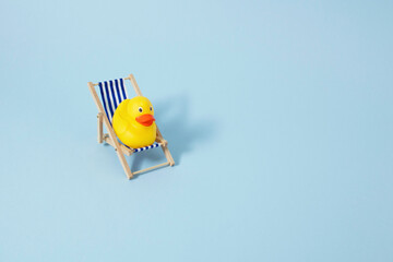 Yellow duck chilling in beach chair on the blue background. Summer vacation concept. 