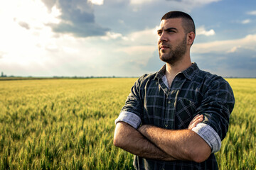Naklejka na ściany i meble Portrait of young farmer standing in a green wheat field at sunset.
