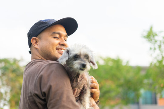 Yong asian man in casual outfit of cheerful with old dog at outdoors. Male playing with her little adopted dog pet and owner having good time together. Hugs and kisses, Love, Care, Friendship
