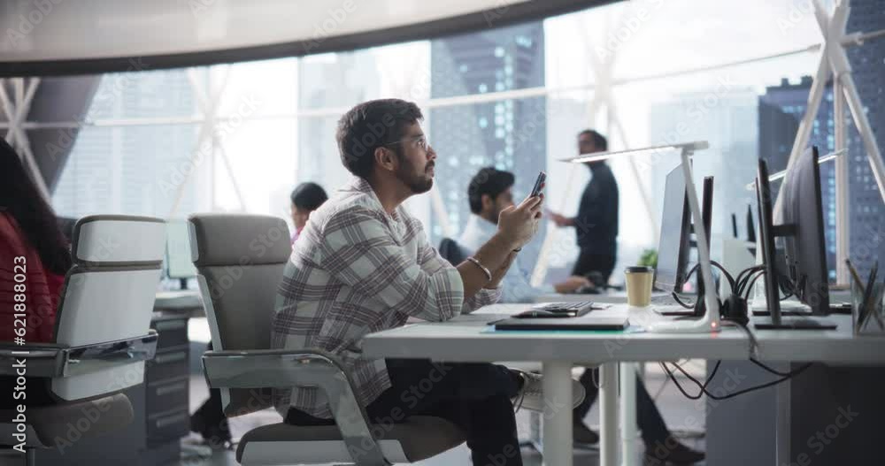 Poster portrait of a handsome indian manager using smartphone while sitting behind a desk in a corporate of