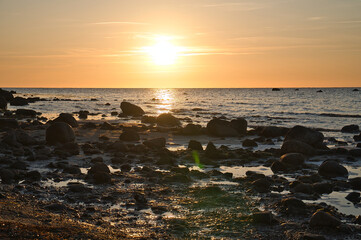 Fototapeta na wymiar Sunset, stone beach with small and large rocks in front of the illuminated sea.