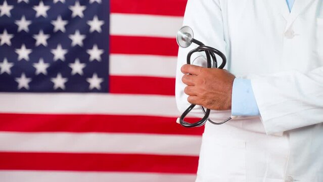 Confident Doctor standing by holding stethoscope in hand in fornt og US flag - concept of US labour day celebration showing with copy space