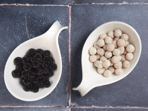 Raw and cooked tapioca balls with different flavors, also known as boba in bubble tea, on gray tile background. An ingredient to make pearl milk tea.