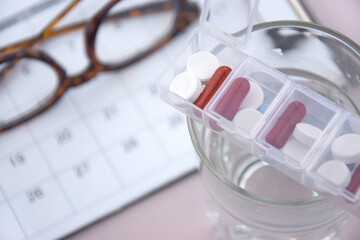 Calendar with pills and non-contact thermometer on light background.