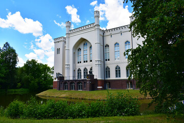 Fototapeta na wymiar Old castle with white walls, arch and high windows. Green trees all around and blue sky. Natural historical park. Poland, Kurnik castle, Poznan, June 2022.