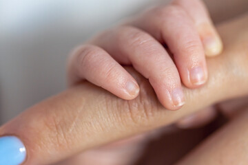 The small hand of a newborn holds the mother's finger.