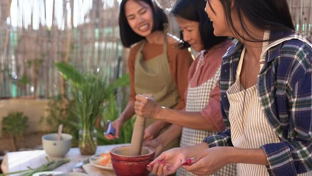 Happy asian mother and adult daughters cooking together traditional thai food at home terrace - Family love and culture concept