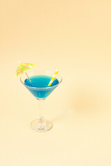 Martini cup concept with blue slime and yellow umbrella on sand colored background. Summer idea.