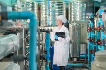Female worker inspecting water bottle on production line in spring water factory