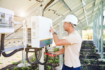 Professional worker checking voltage on solar inverter. Male using current probe to measure output...