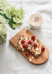Delicious beautiful breakfast, snack, dessert - toast with peanut paste, banana, raspberry and chocolate, cappuccino, bouquet of hydrangeas on a white background, top view