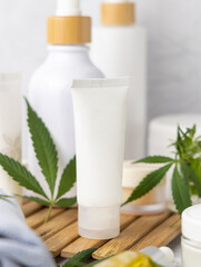 Obraz na płótnie Canvas White blank cream tube near green cannabis leaves close up, CBD cosmetic, mockup