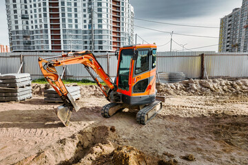 A small mini excavator is working on a construction site. Close-up. View from above. Work in cramped conditions. Excavation. - obrazy, fototapety, plakaty