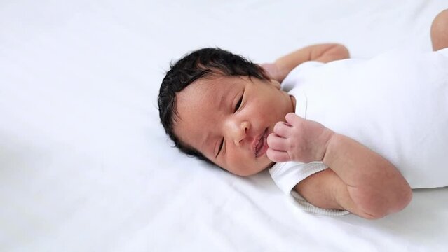 portrait of a newborn black African-American baby yawning or reading to eat, a small dark-skinned baby close-up on the bed in the bedroom has just woken up or is falling asleep in a white bodysuit