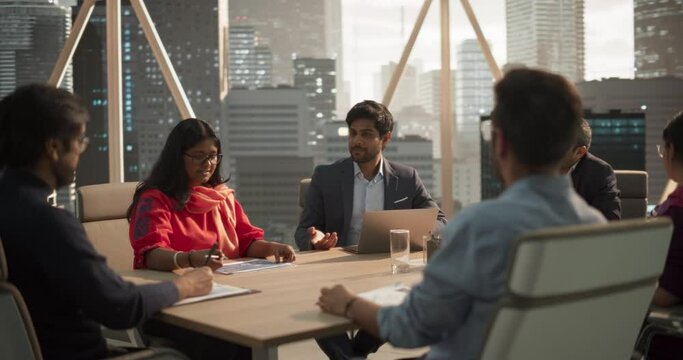 Young Indian Project Manager Makes a Business Presentation for a Diverse Creative Team in a Meeting Room in an Agency. South Asian Colleagues Gathered Around a Conference Table. Arc Shot
