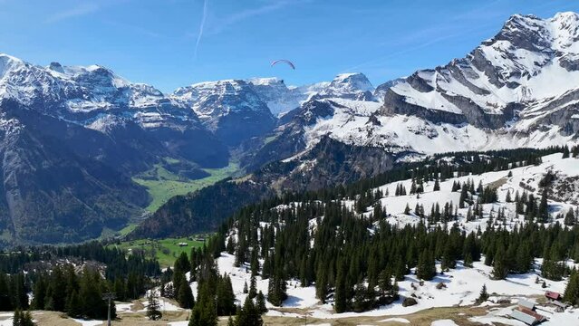 Aerial view of a person paragliding among the mountains in wintertime with snow, Braunwald, Switzerland.