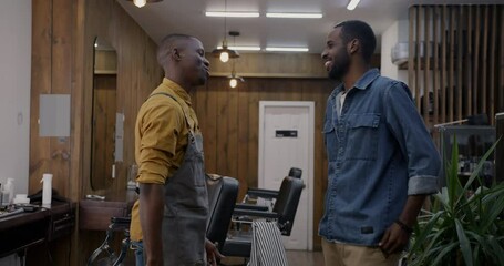 Two cheerful African American men barber and client meeting shaking hands and talking in barbershop. Hair salon and young people concept.