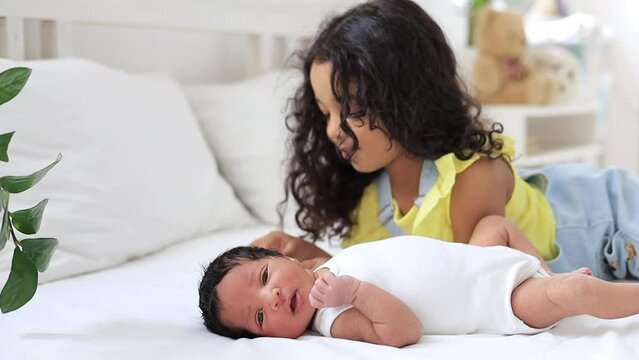 sister kisses hands and strokes the tummy of a newborn African-American baby, black brother and sister close-up lying on the bed in the bedroom after waking up or playing together